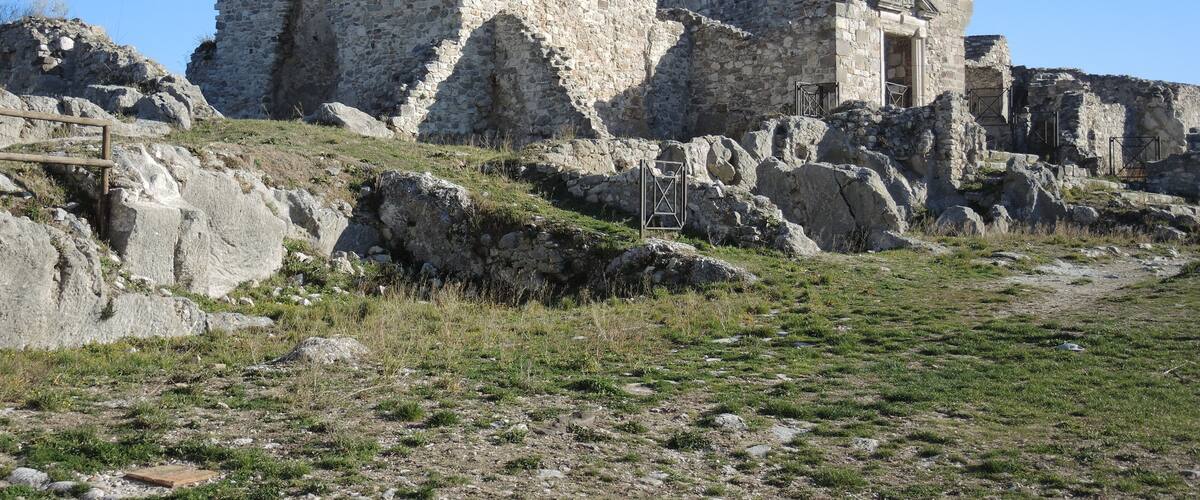 Vestiges d’une ancienne construction en pierre, avec une structure centrale imposante et des bâtiments plus petits qui l’entourent.