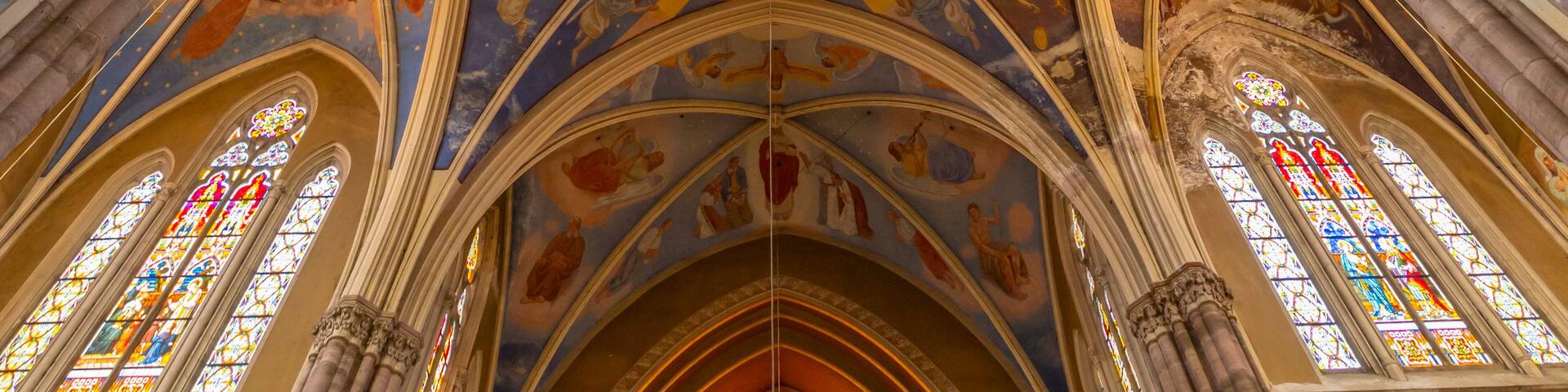 A cathedral's interior with a high vaulted ceiling, stained glass windows, and religious frescoes.