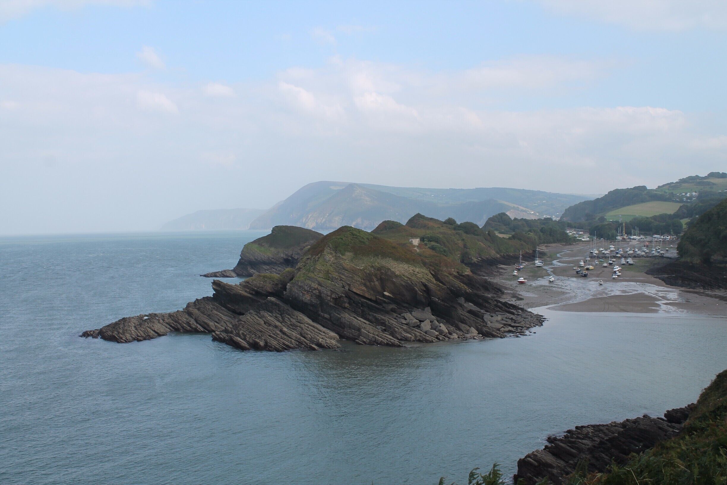 A coastal landscape with rocky cliffs, a beach, and a village in the distance.