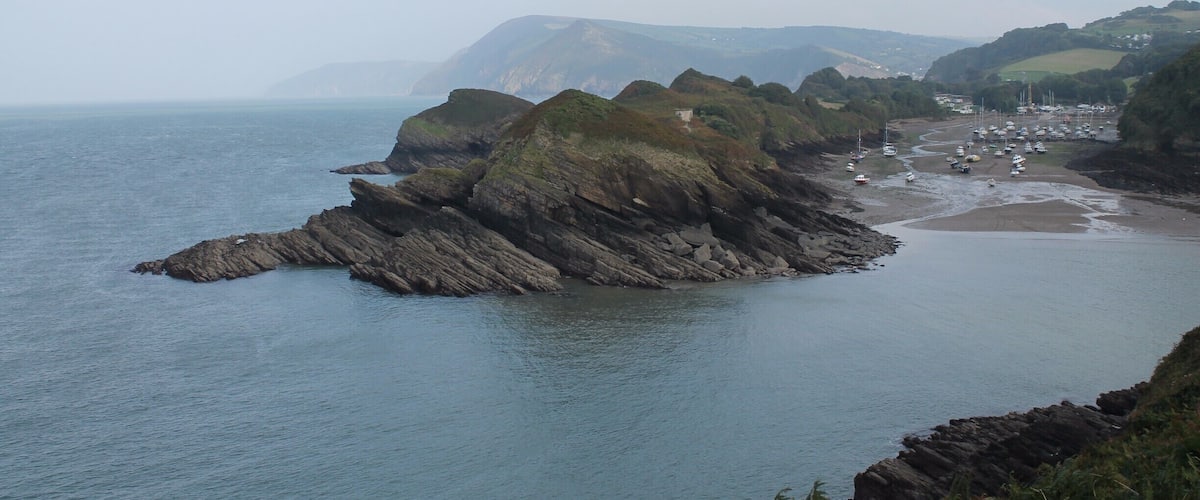 A coastal landscape with rocky cliffs, a beach, and a village in the distance.