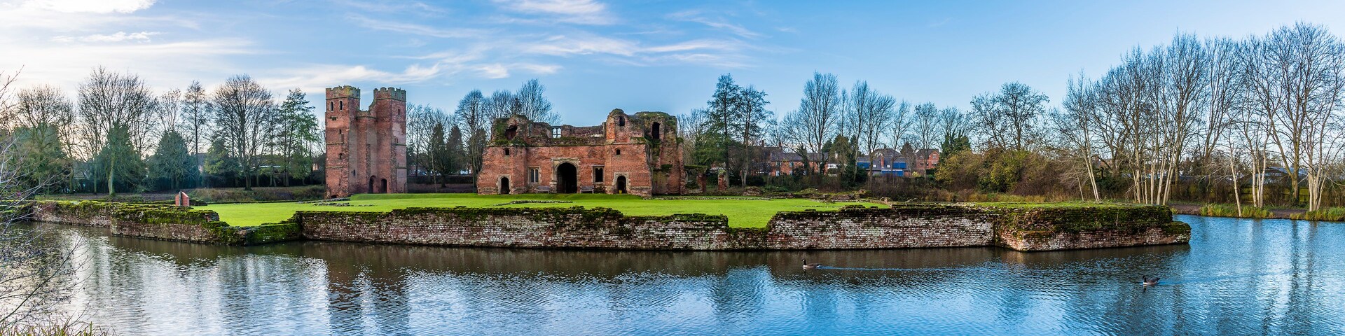 Les ruines d’un château historique, entourées d’un fossé et d’arbres.