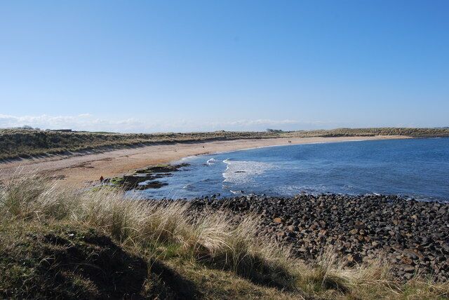 A coastal landscape with a sandy beach, a rocky shoreline, and a clear blue sky.