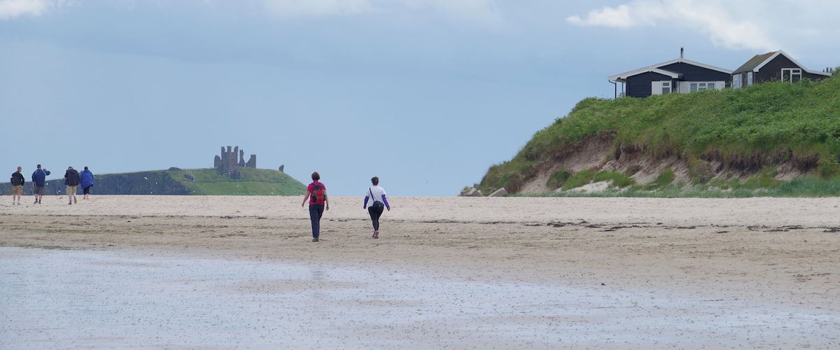 A beach with people walking, a grassy hill with a house, and a distant castle.