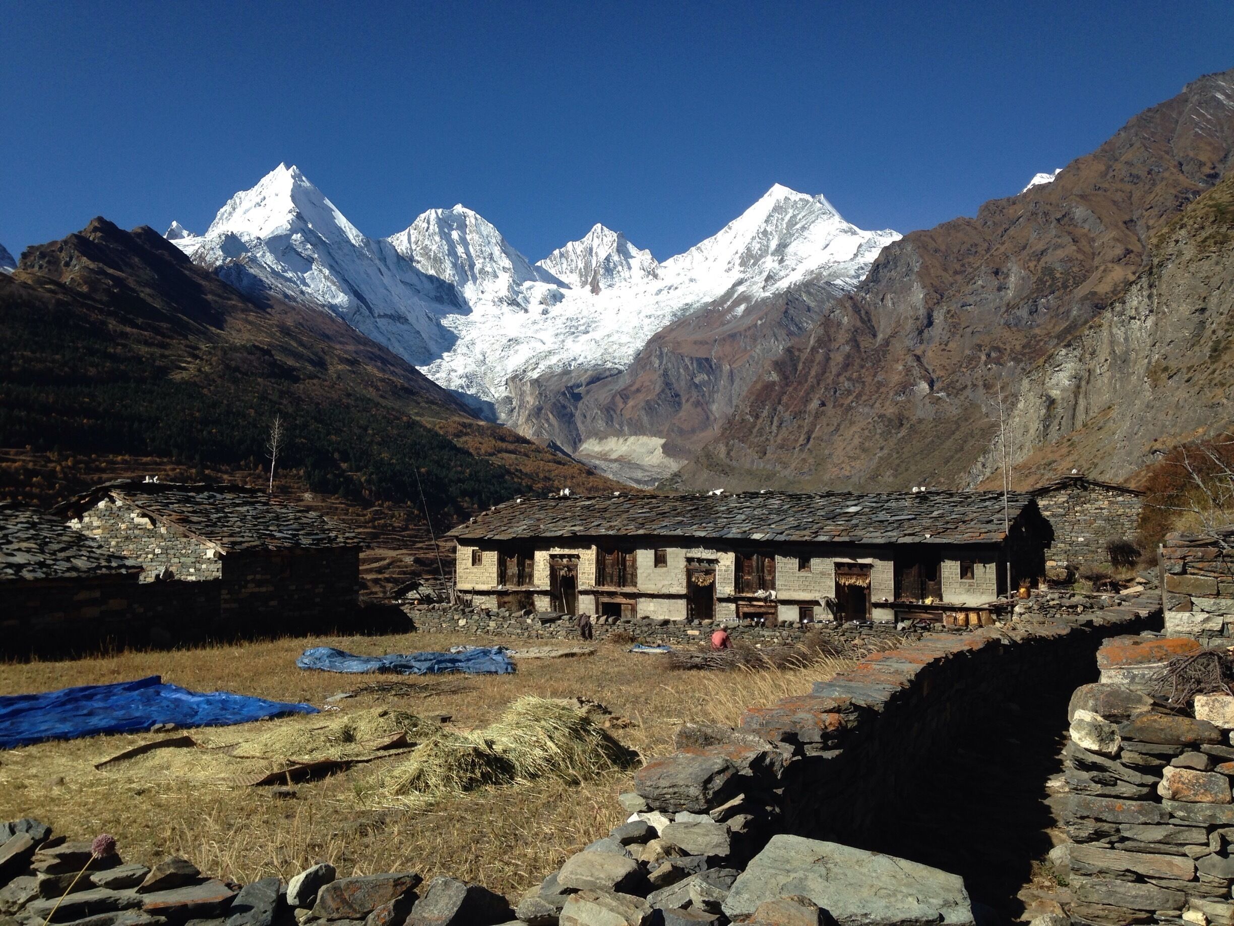 A traditional stone building in a mountainous area with snow-capped peaks in the background.