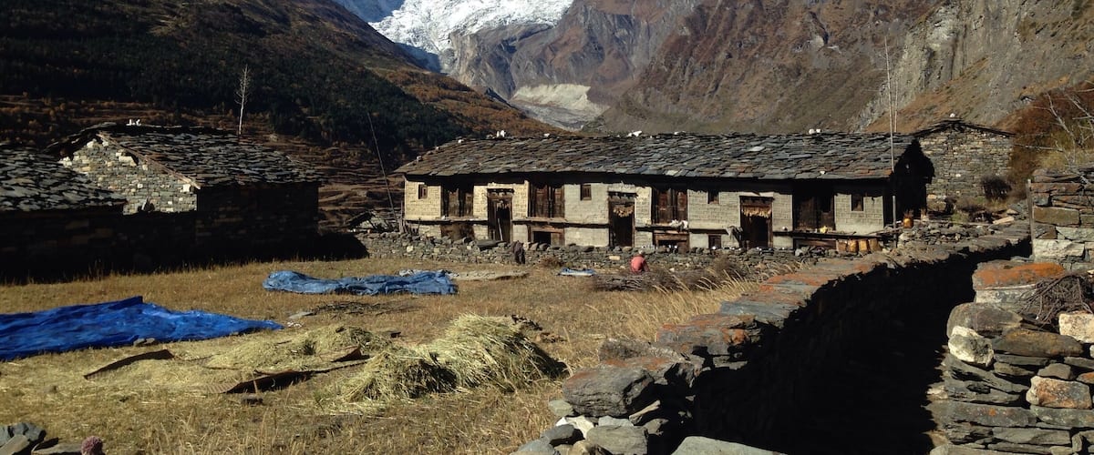 A traditional stone building in a mountainous area with snow-capped peaks in the background.