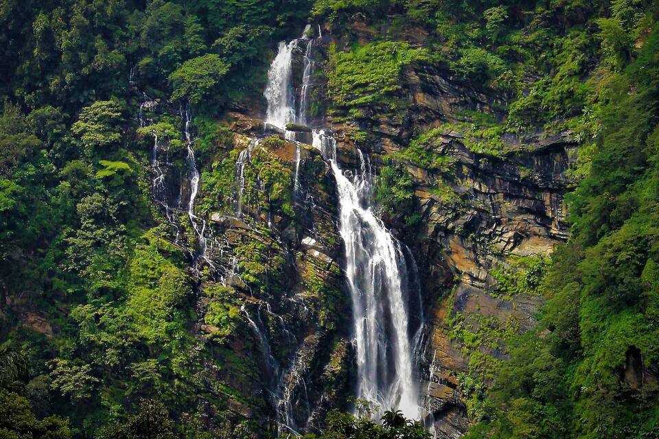 A multi-tiered waterfall surrounded by dense green forest.