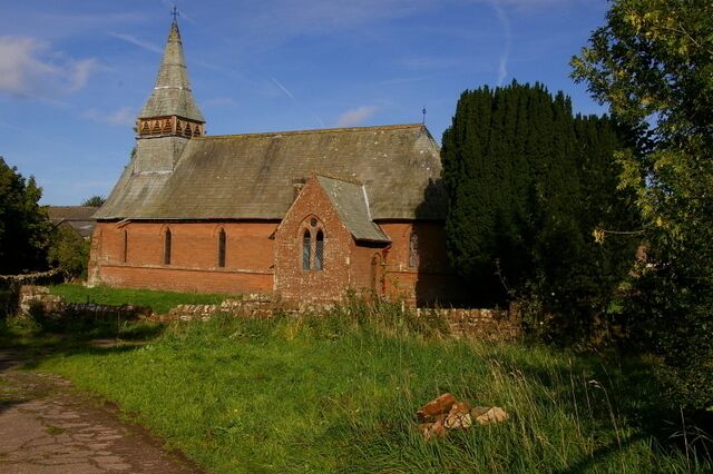 A church with a tall steeple and a brick facade, surrounded by greenery and a stone path.
