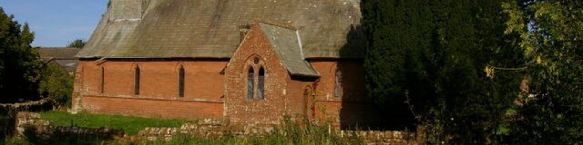 A church with a tall steeple and a brick facade, surrounded by greenery and a stone path.