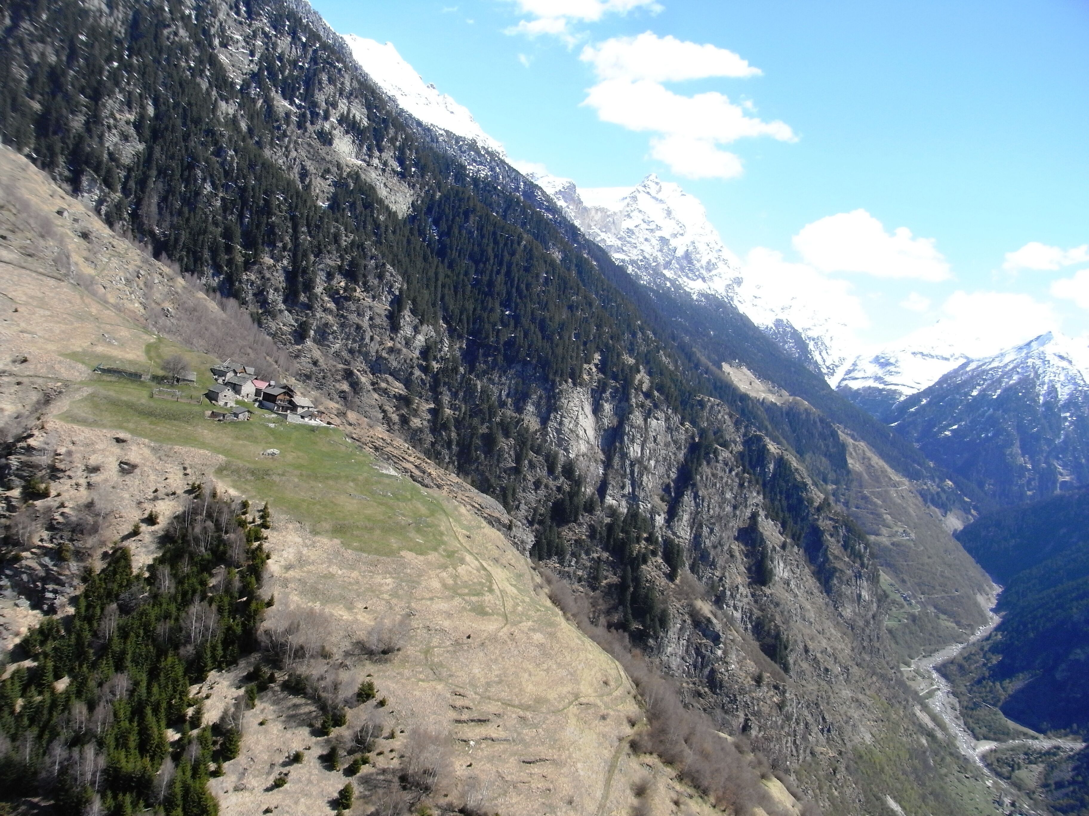 A mountainous landscape with a valley, a small settlement, and snow-capped peaks.