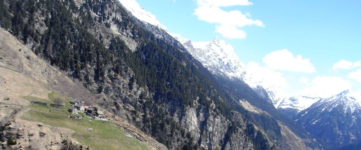 A mountainous landscape with a valley, a small settlement, and snow-capped peaks.