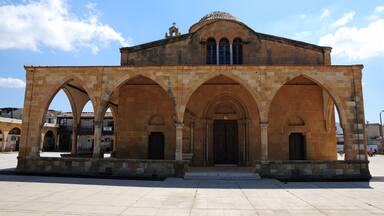 A historic building with a central archway and three side arches, surrounded by a paved plaza.