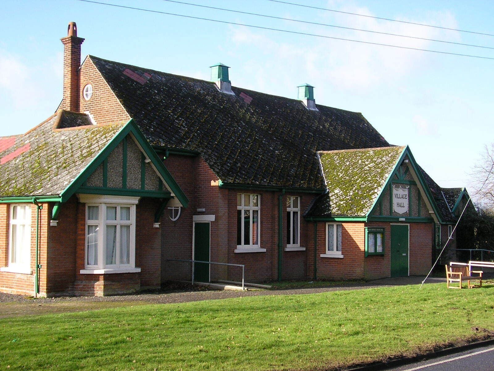 A traditional brick building with green trim and a tiled roof, labeled as a village hall.