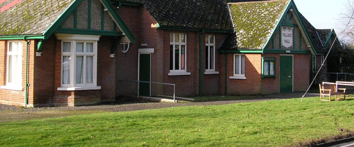 A traditional brick building with green trim and a tiled roof, labeled as a village hall.