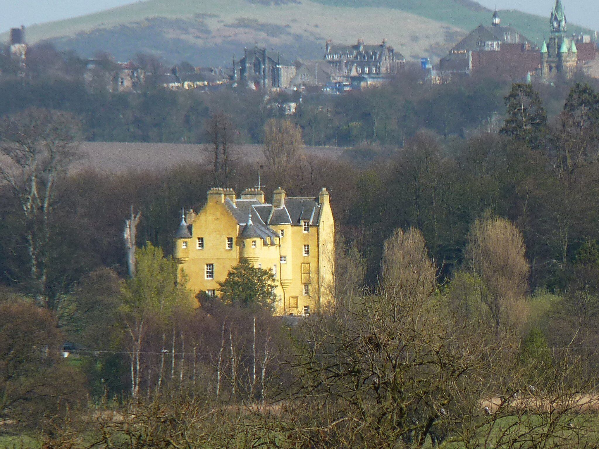 A large yellow building surrounded by trees and hills.