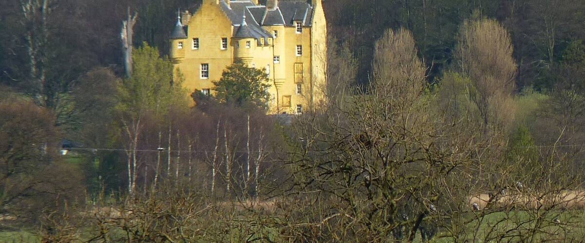 A large yellow building surrounded by trees and hills.