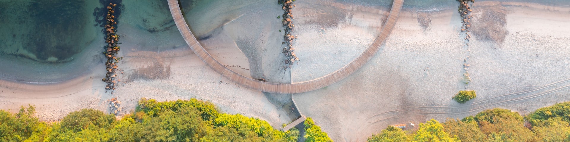 An aerial view of a circular wooden structure in a body of water surrounded by a forested area.