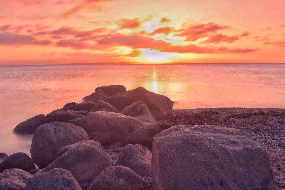 Un capvespre sobre un mar tranquil amb roques grans en primer pla.
