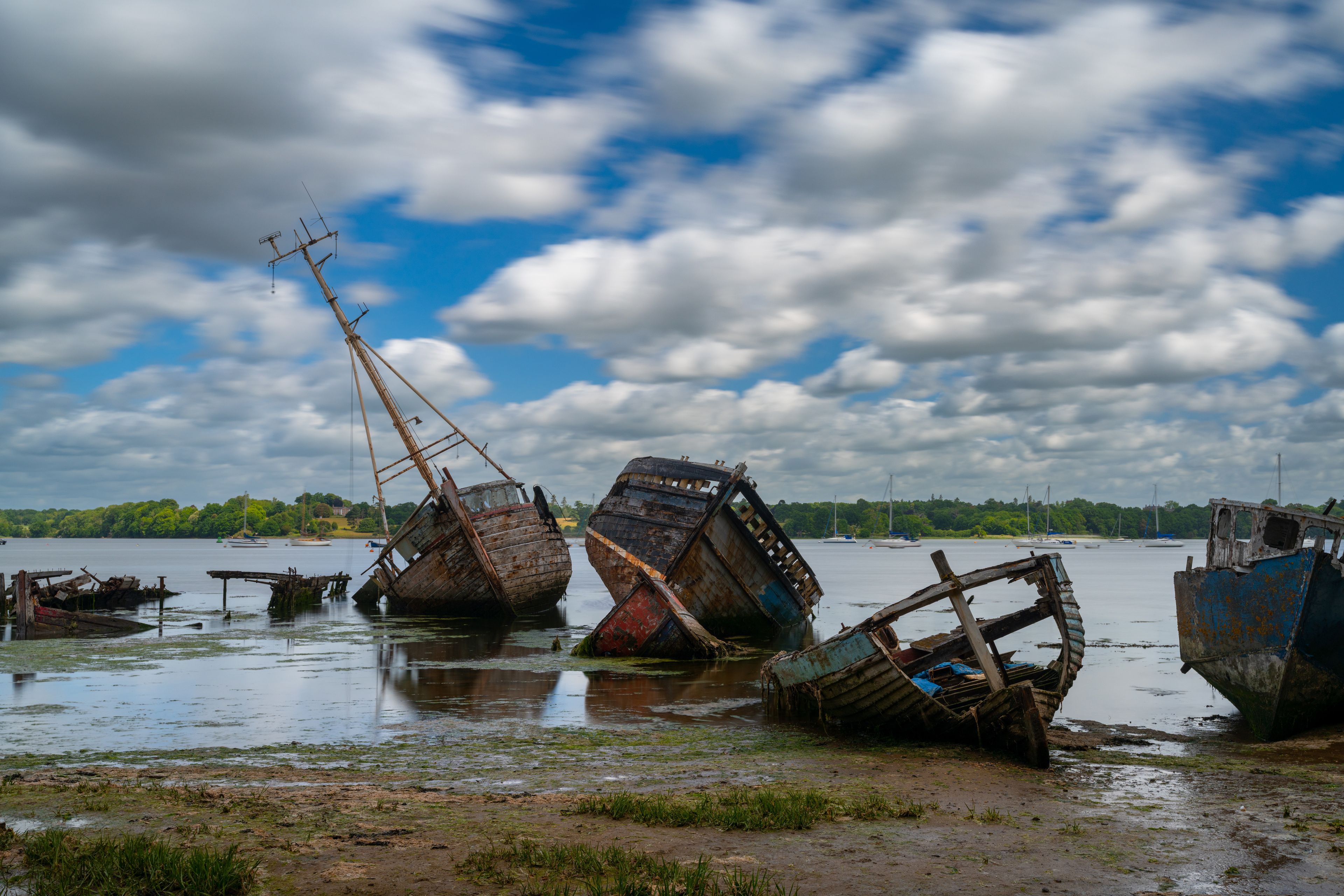 A group of sunken ships in a calm body of water with a cloudy sky.