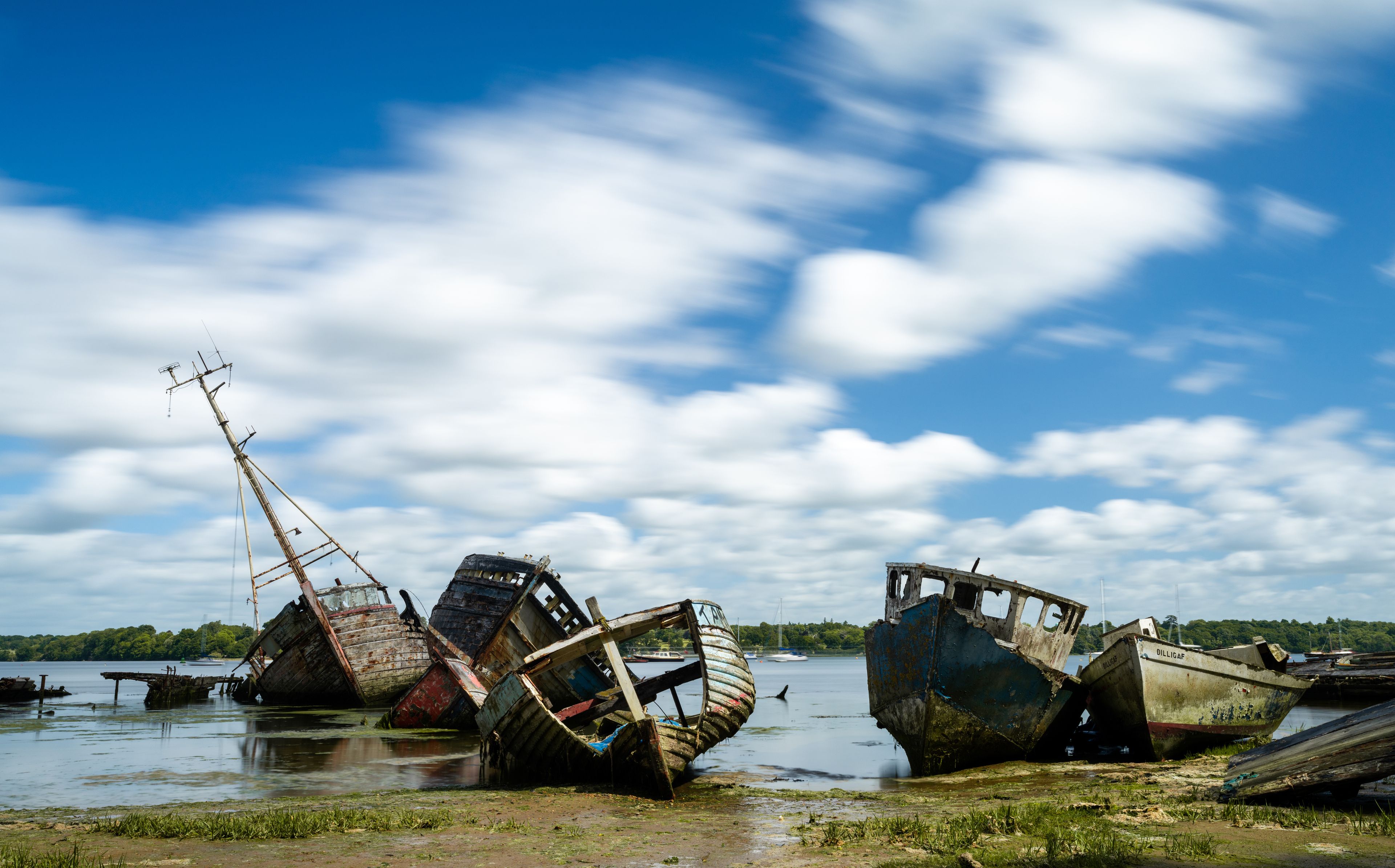 A row of sunken boats on a riverbank with a clear sky.