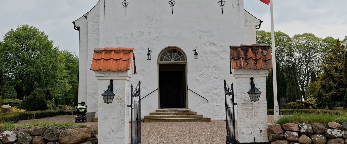 A white church with a steep roof and a flagpole.