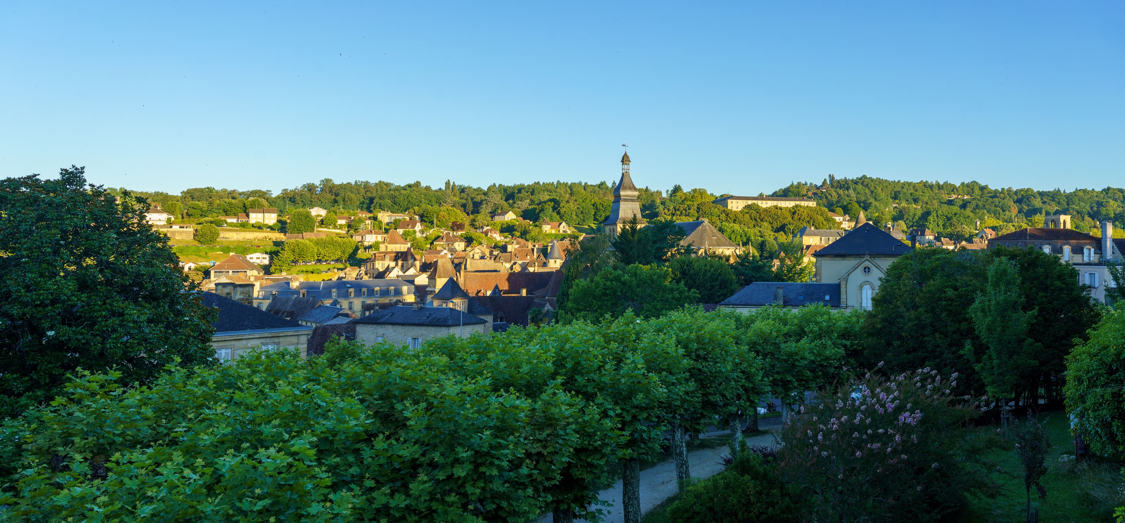 A town with historic buildings, a prominent church tower, and lush greenery.