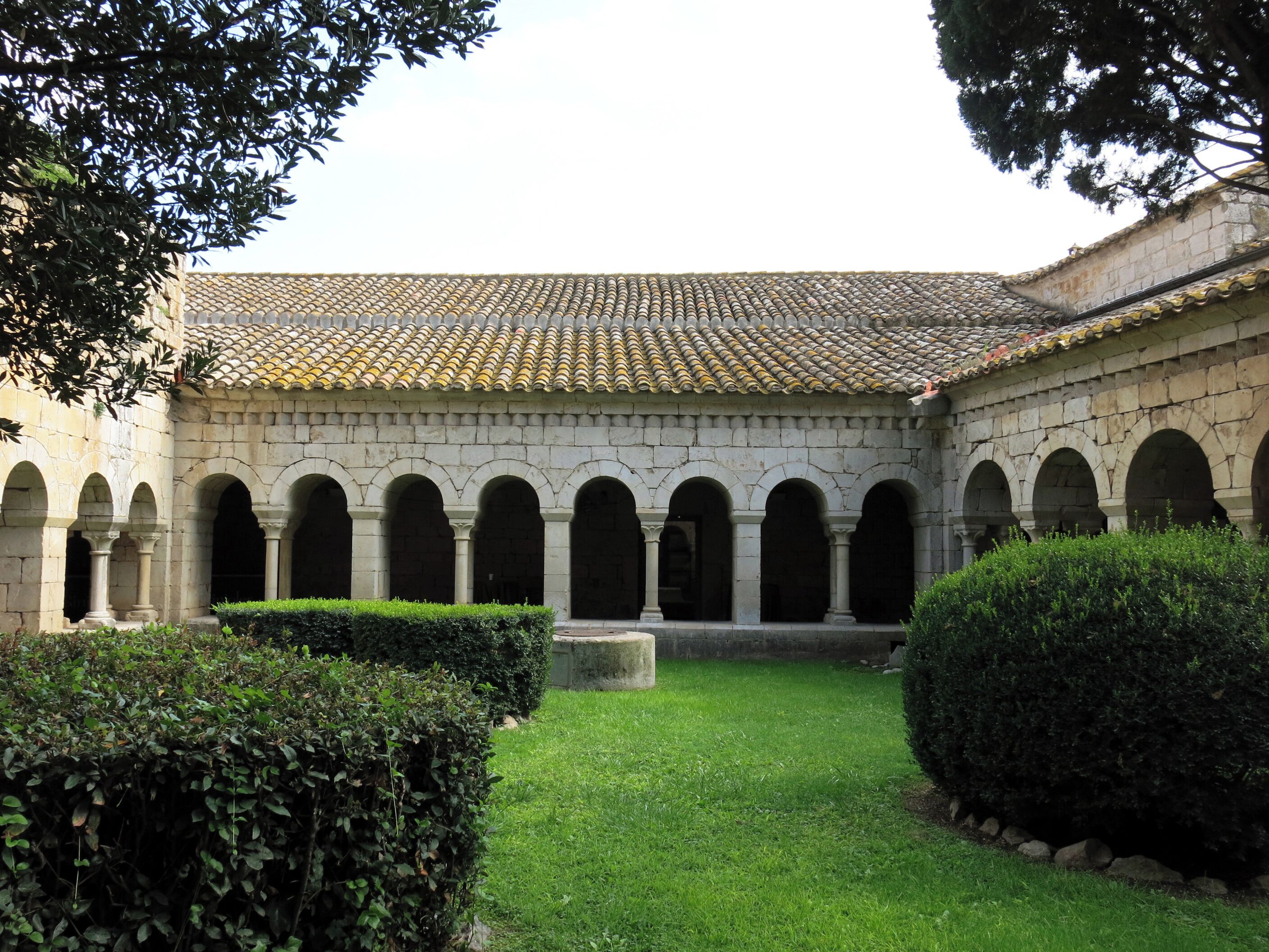 A courtyard with a tiled roof, stone arches, and green hedges.