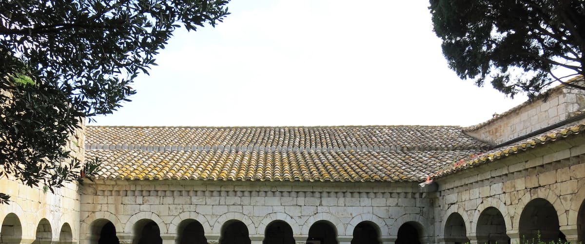 A courtyard with a tiled roof, stone arches, and green hedges.