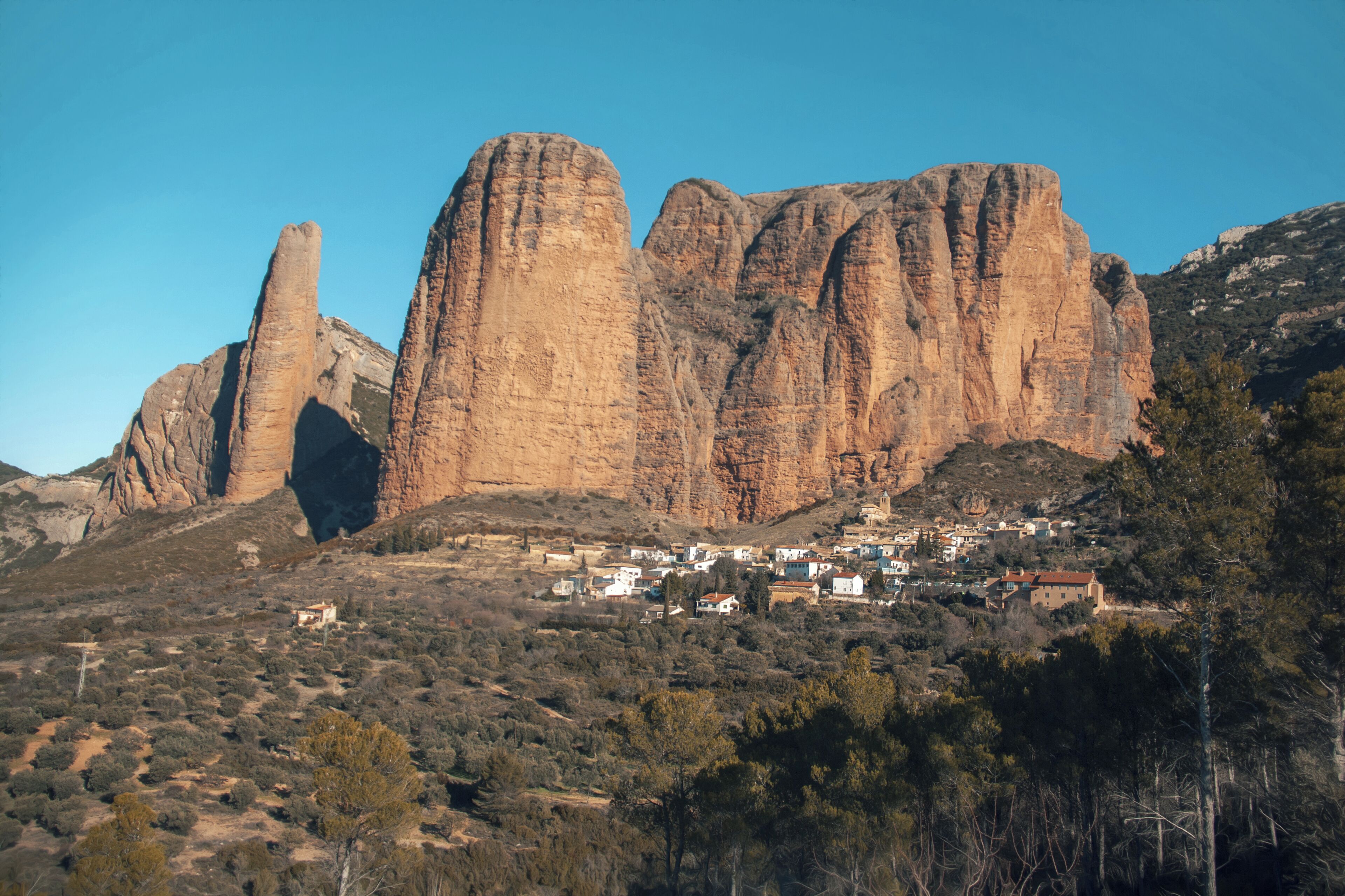 A mountainous landscape with prominent rock formations and a small village nestled at the base.