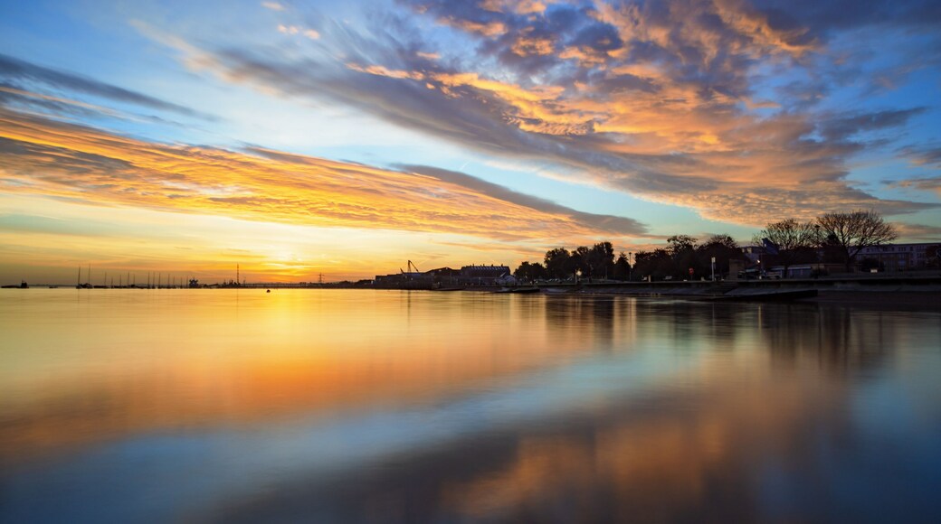 Un atardecer sobre una masa de agua tranquila con el horizonte de una ciudad a lo lejos.