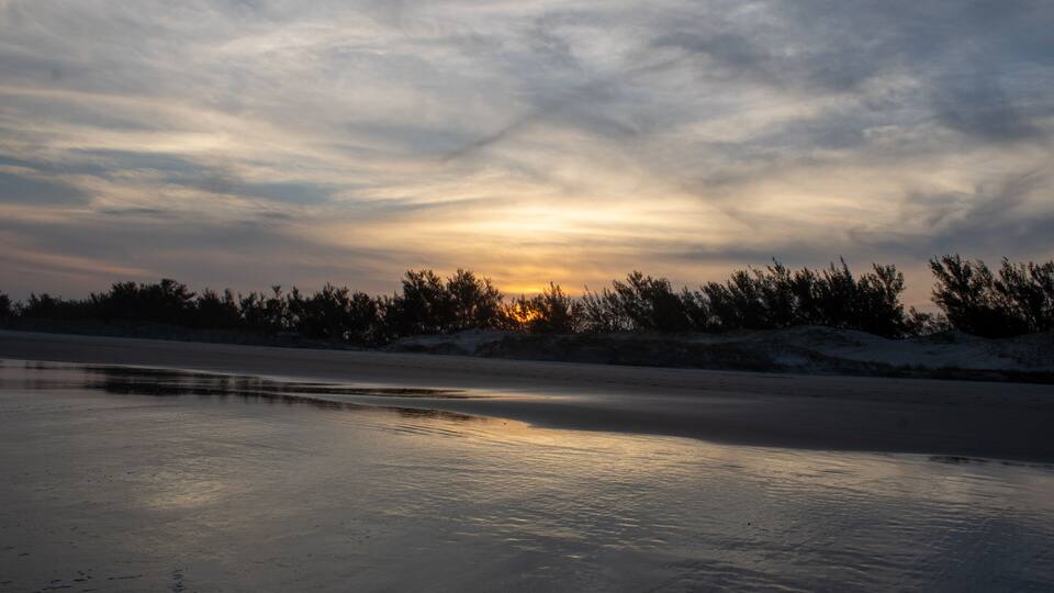 A frozen lake with a sunset in the background and trees silhouetted against the sky.