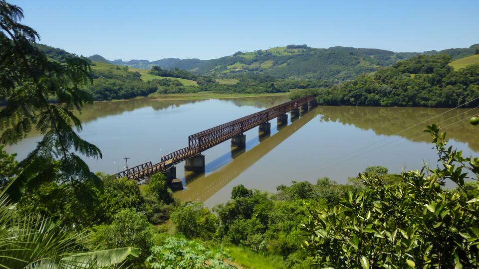 A bridge over a calm river surrounded by lush greenery and hills.