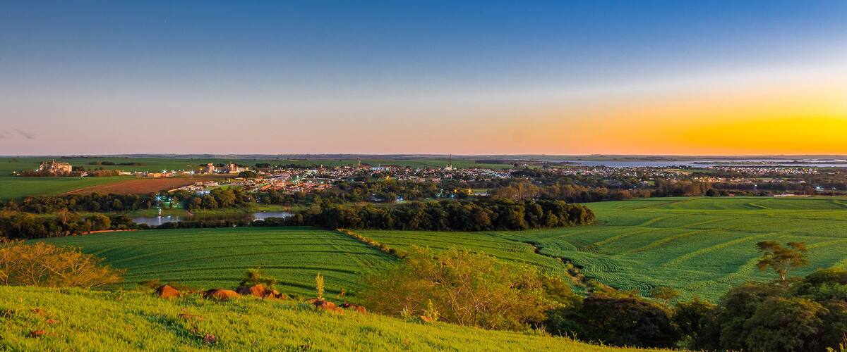 A rural landscape with fields, a small town, and a sunset.