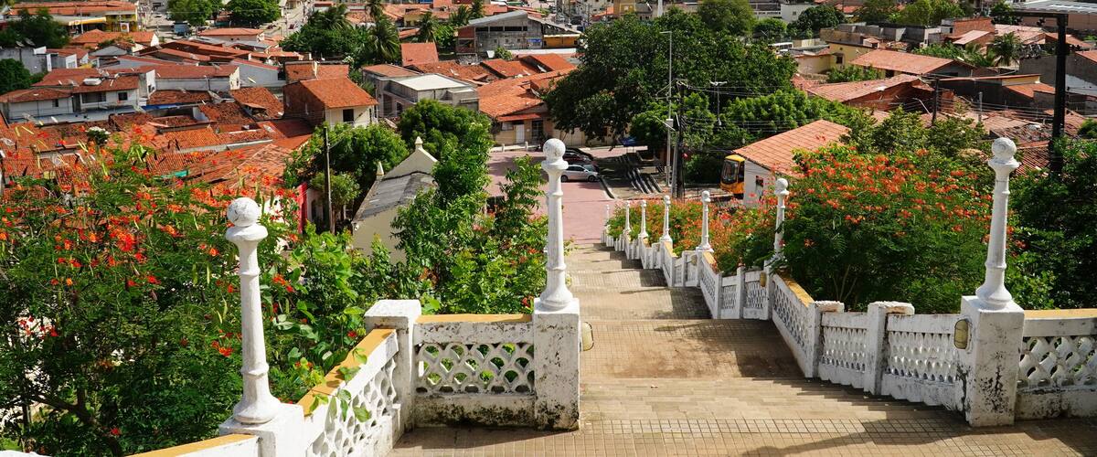 A town with red-roofed buildings, a church, and lush green hills in the background.