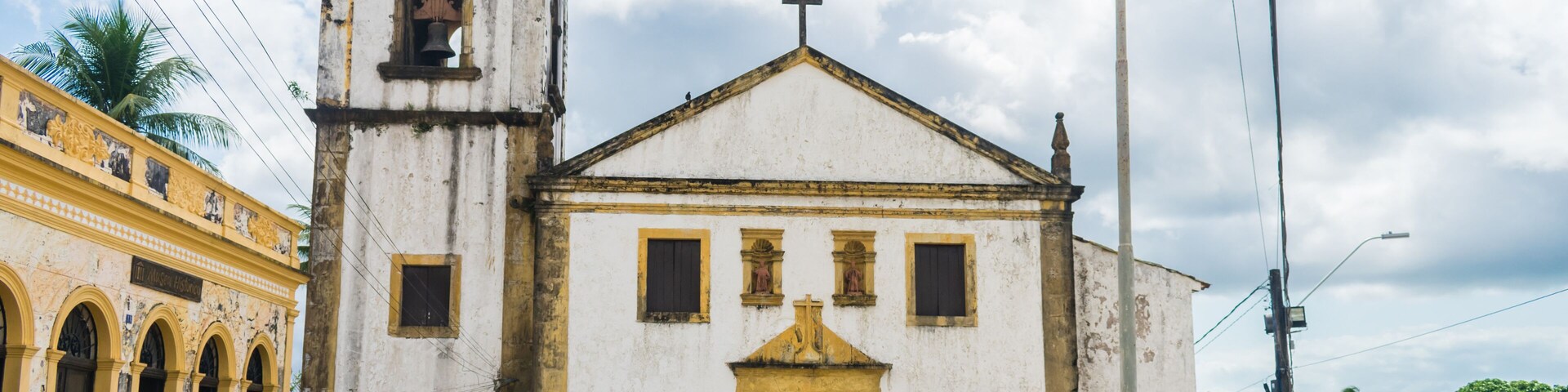 Una iglesia blanca con un campanario y una cruz en la parte superior, rodeada de palmeras y un cielo despejado.