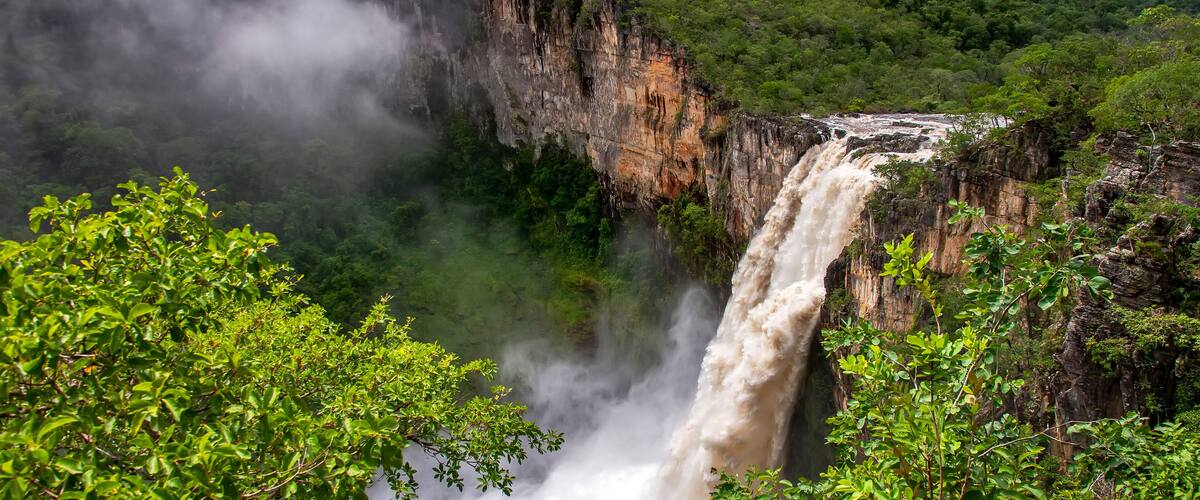 A waterfall cascading down a steep cliff surrounded by lush greenery.