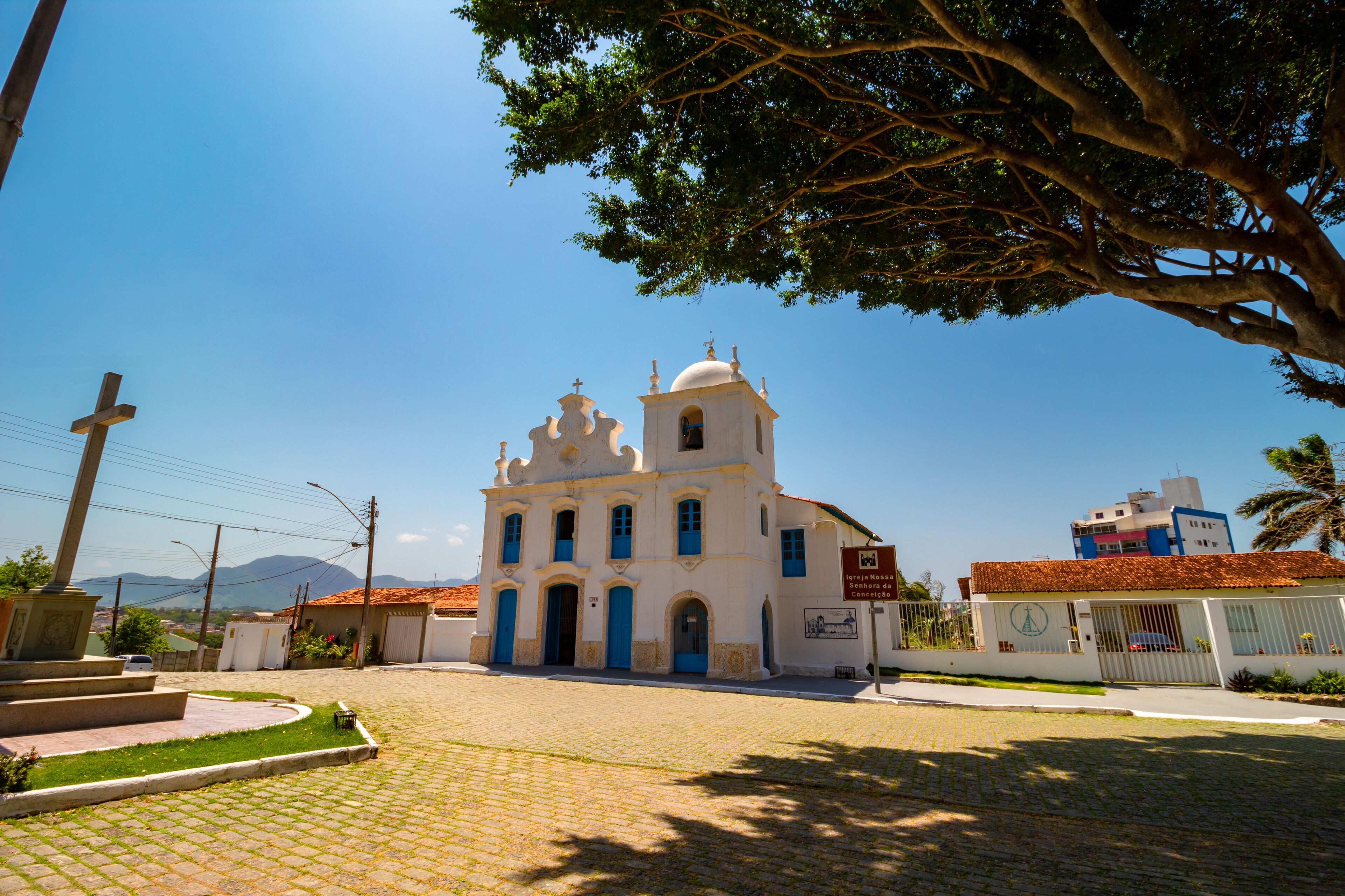 A white church with blue doors and a bell tower, surrounded by a cobblestone street and greenery.