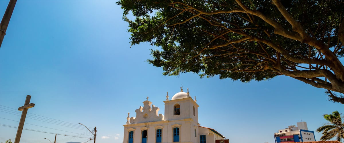 A white church with blue doors and a bell tower, surrounded by a cobblestone street and greenery.