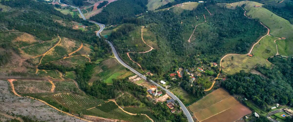 An aerial view of a winding road through a hilly landscape with fields and scattered buildings.
