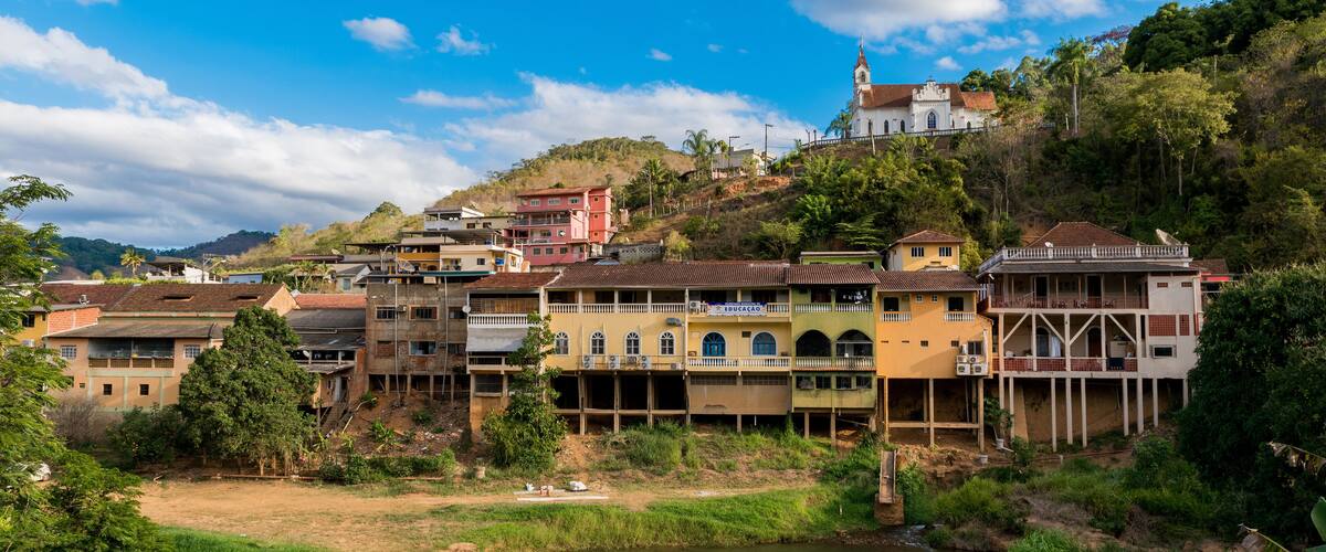 A riverside town with colorful buildings, a church on a hill, and lush greenery.