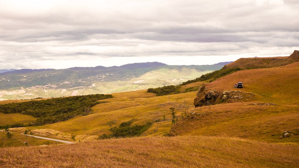 A hilly landscape with a winding road and a vehicle on a dirt path.