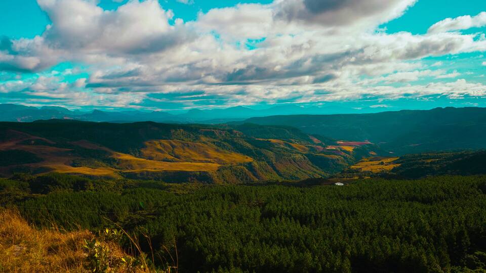 A mountainous landscape with dense forests and rolling hills under a partly cloudy sky.