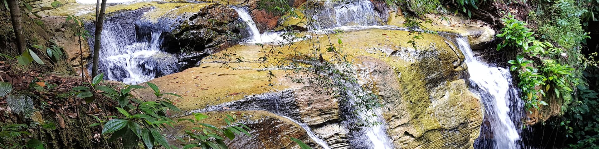 A multi-tiered waterfall surrounded by lush greenery and moss-covered rocks.