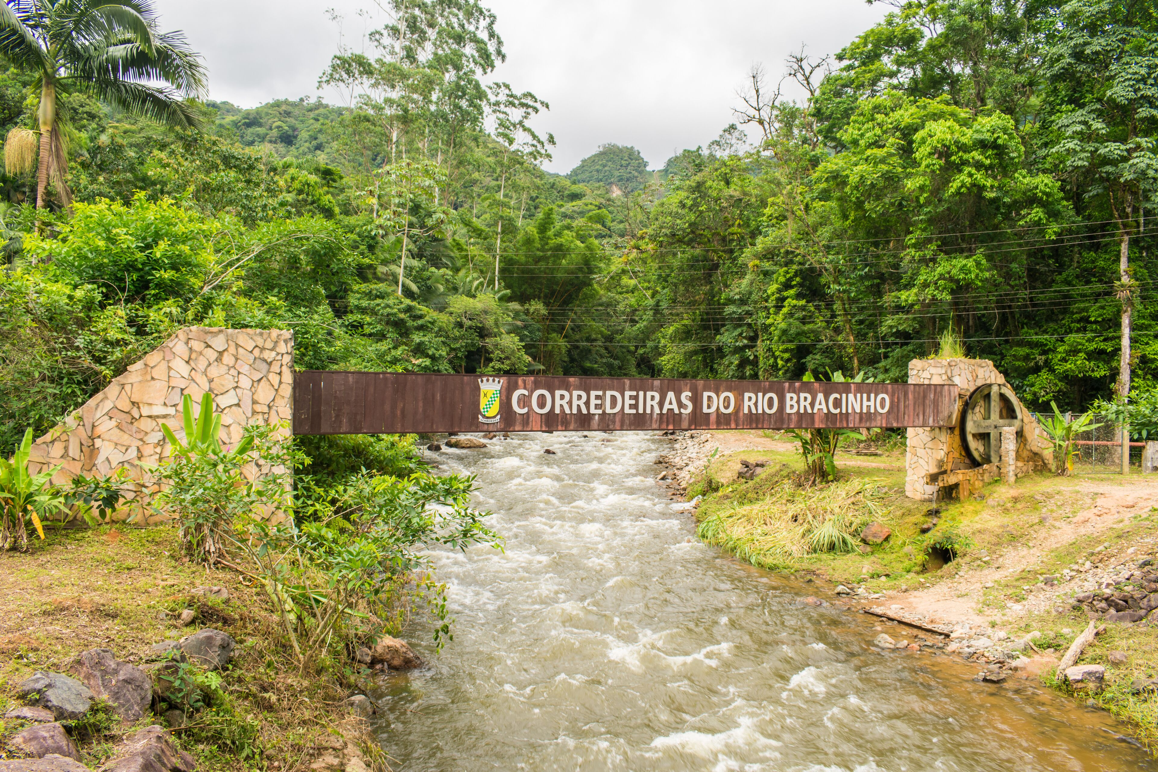 A river flowing under a bridge with a sign that reads "CORREDEIRAS DO RIO BRACINHO".