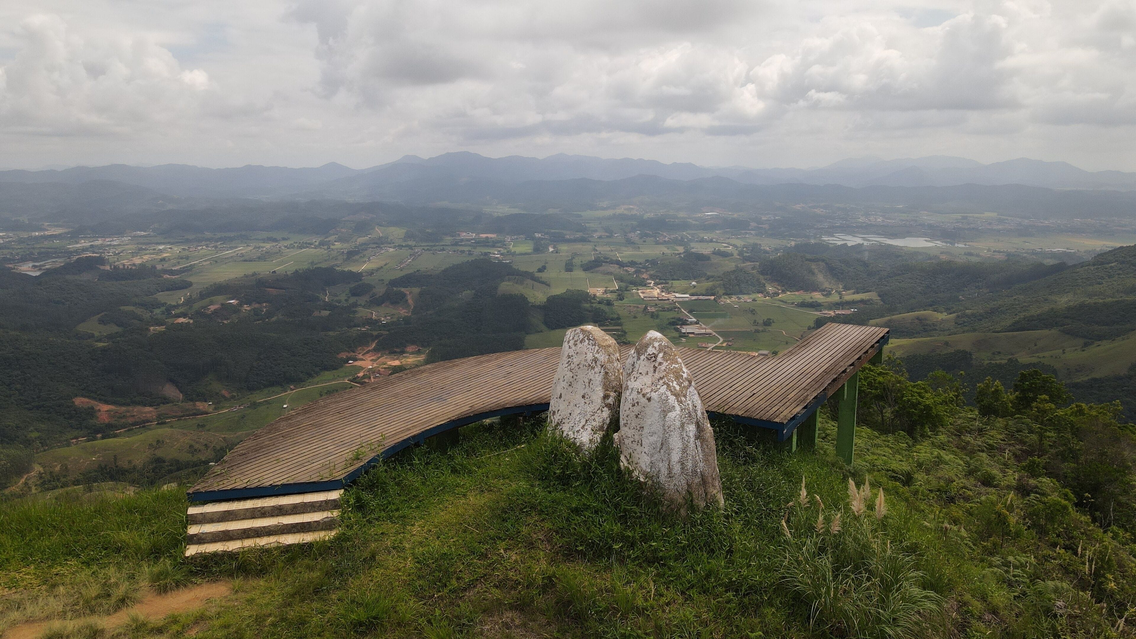 A wooden viewing platform with a curved roof overlooking a valley with distant mountains.