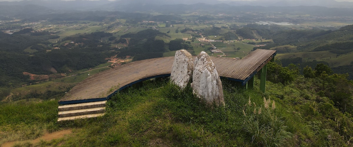 A wooden viewing platform with a curved roof overlooking a valley with distant mountains.