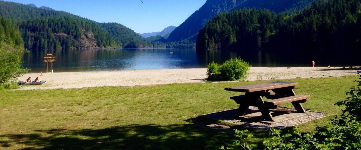 A picnic table by a lake with mountains in the background.