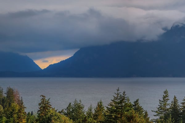 Une chaîne de montagnes avec un lac au premier plan et une zone boisée.