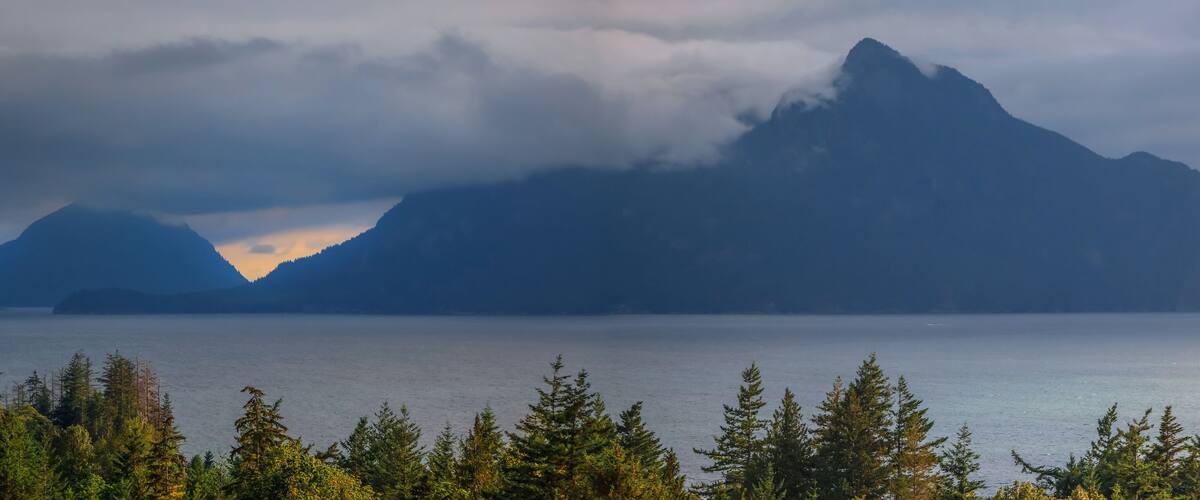 A mountain range with a lake in the foreground and a forested area.