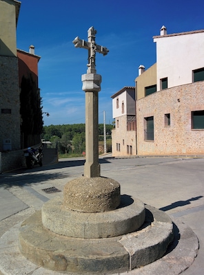 Una cruz de piedra en una plaza rodeada de edificios.