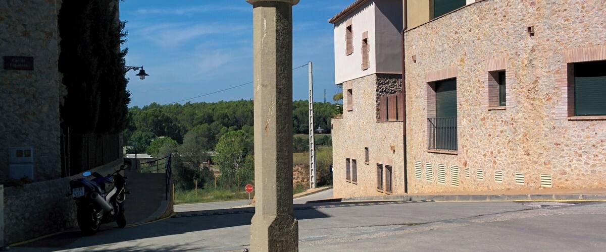 A stone cross in a plaza surrounded by buildings.